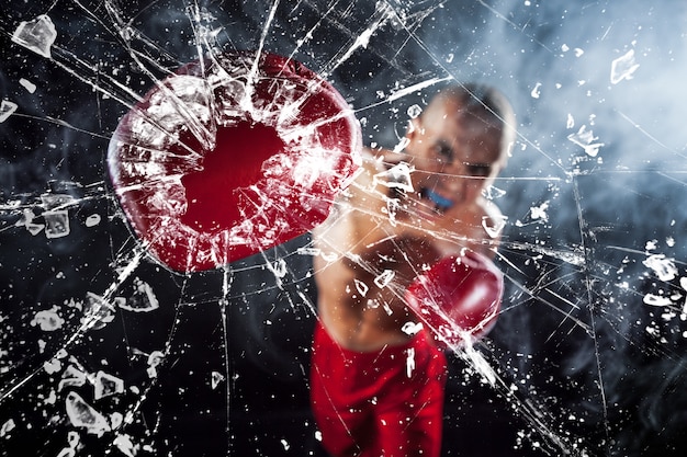 Il pugile che schiaccia un bicchiere. Il kickboxing giovane atleta maschio su un fumo blu