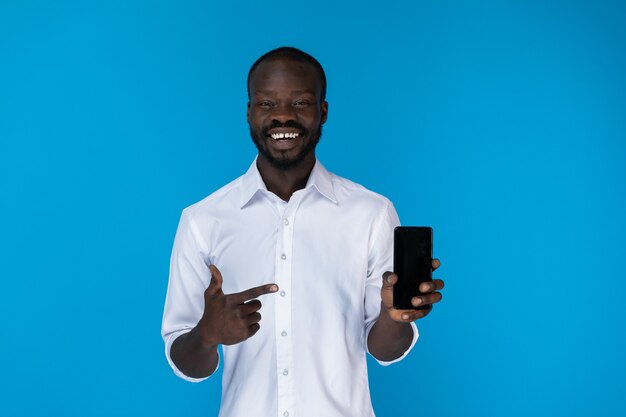 Il ragazzo afroamericano barbuto sta mostrando il cellulare in camicia bianca