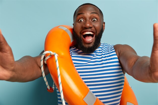 Il ragazzo afroamericano felice e allegro fissa con felicità la telecamera, fa selfie, posa con lifering