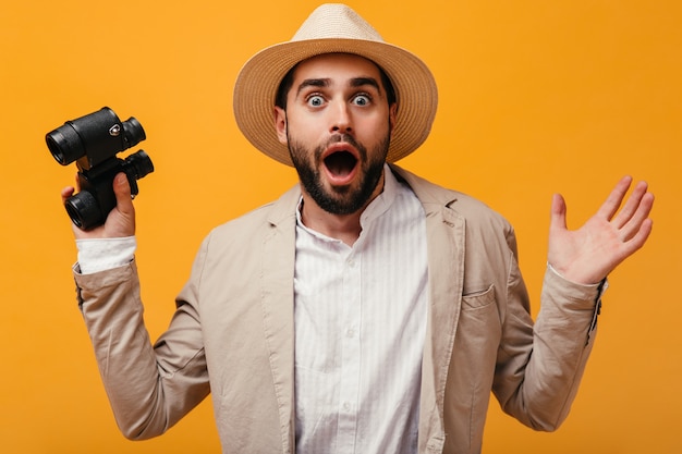 Il ragazzo con il cappello sembra scioccato davanti alla telecamera e tiene in mano un binocolo