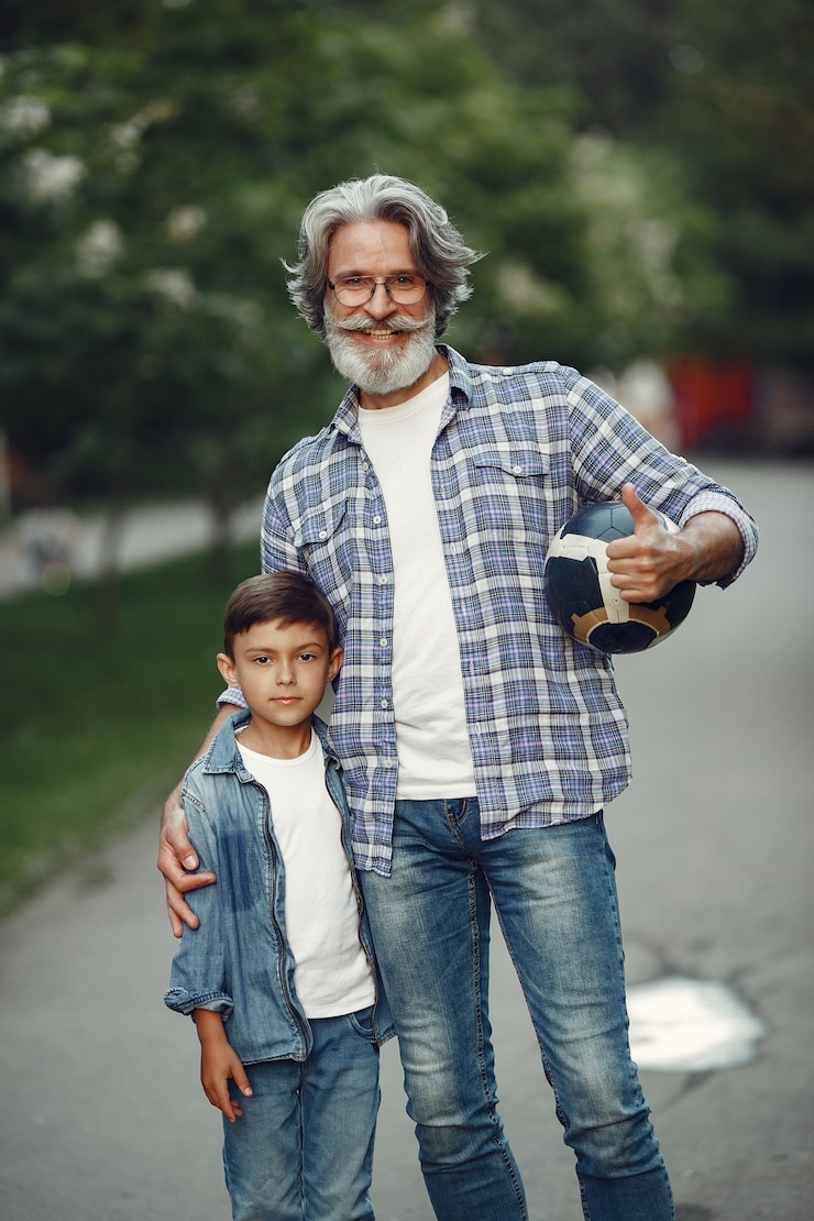 Foto gratuito il ragazzo e il nonno stanno camminando nel parco. uomo anziano che gioca con il nipote. famiglia che gioca con una palla.