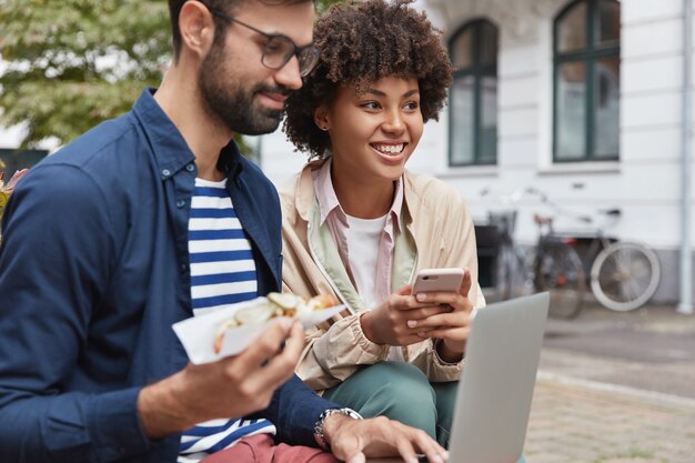 Il ragazzo e la ragazza felici di razze diverse utilizzano gadget moderni per la comunicazione online