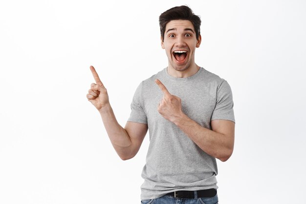 Il ragazzo felice eccitato indica da parte e ride L'uomo allegro mostra la pubblicità sul lato sinistro si erge su sfondo bianco