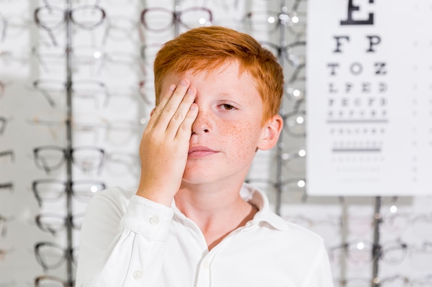 Il ragazzo sveglio ha coperto il suo occhio di mano che sta nella clinica di ottica