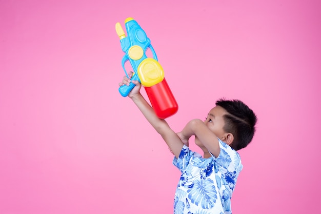 Il ragazzo tiene una pistola ad acqua su uno sfondo rosa.