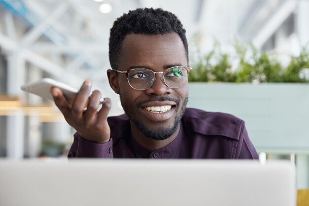 Il receptionist maschio africano soddisfatto invia informazioni per i clienti tramite smart phone, utilizza Internet ad alta velocità.