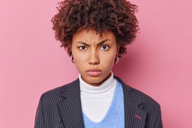 Il regista femminile serio e rigoroso guarda attentamente la telecamera indossa una giacca elegante ascolta le pose del collega su sfondo rosa. Insegnante dispiaciuta stanca dopo una giornata di lavoro arrabbiata con qualcuno