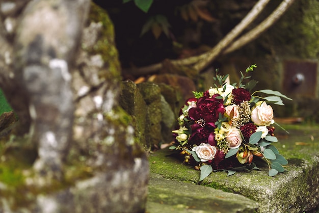 Il ricco bouquet da sposa rosso autunnale giace sulle orme di pietra