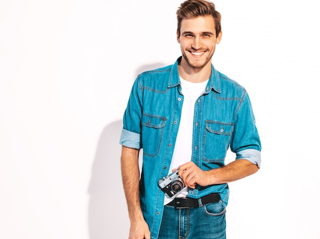 Il ritratto dei vestiti d'uso d'uso dei jeans dell'estate sorridente bello. Maschera di presa maschio di modello sulla vecchia macchina fotografica d'annata della foto.