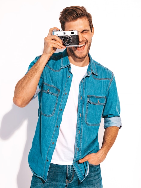 Il ritratto dei vestiti d'uso d'uso dei jeans dell'estate sorridente bello. Maschera di presa maschio di modello sulla vecchia macchina fotografica d'annata della foto.