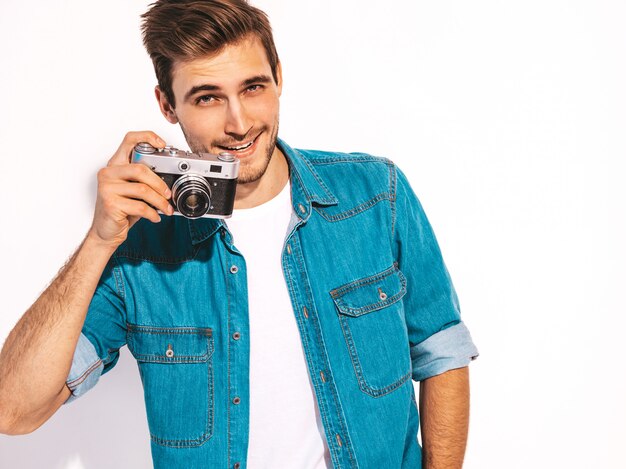 Il ritratto dei vestiti d'uso d'uso dei jeans dell'estate sorridente bello. Maschera di presa maschio di modello sulla vecchia macchina fotografica d'annata della foto.