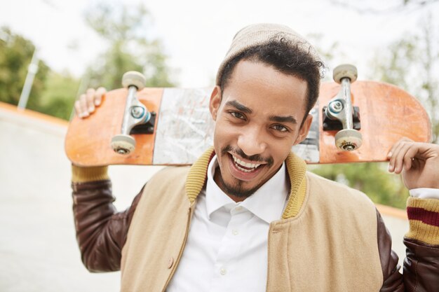 Il ritratto del giovane adolescente positivo pratica lo skateboard all'aperto, ha un'espressione felice