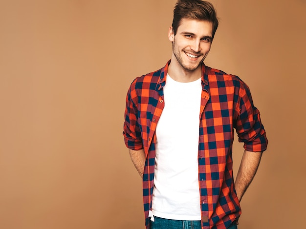 Il ritratto del modello alla moda sorridente bello del giovane si è vestito in camicia a quadretti rossa. Posa di moda uomo