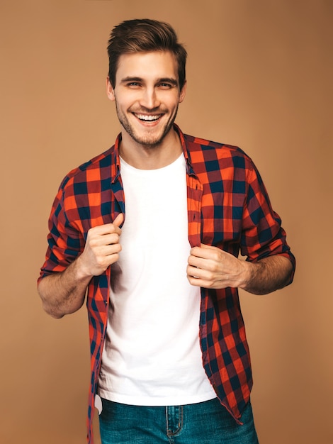 Il ritratto del modello alla moda sorridente bello del giovane si è vestito in camicia a quadretti rossa. Posa di moda uomo