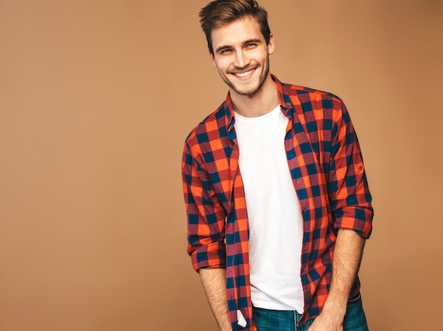 Il ritratto del modello alla moda sorridente bello del giovane si è vestito in camicia a quadretti rossa. Posa di moda uomo