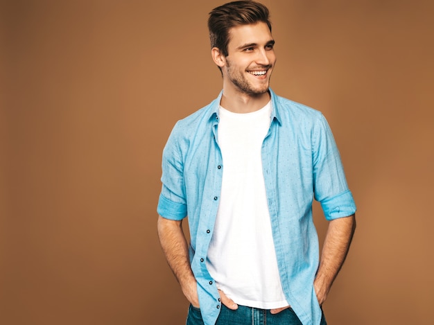 Il ritratto del modello alla moda sorridente bello del giovane si è vestito in vestiti blu della camicia. Posa di moda uomo