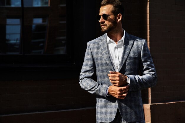 Il ritratto del modello bello sexy dell'uomo d'affari di modo si è vestito in vestito a quadretti elegante che posa sul fondo della via. metrosexual