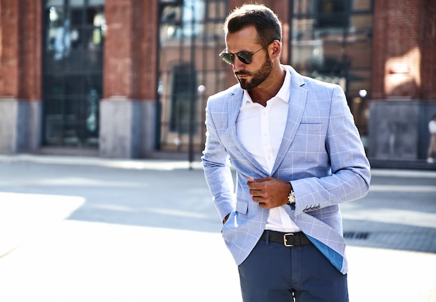 Il ritratto del modello bello sexy dell'uomo d'affari di modo si è vestito in vestito blu elegante che posa sul fondo della via. metrosexual