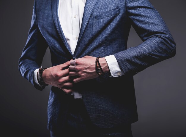 il ritratto del modello dell'uomo d'affari alla moda dei pantaloni a vita bassa alla moda bello si è vestito in vestito blu elegante che posa sul gray.