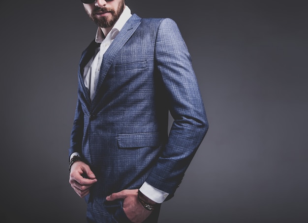 il ritratto del modello dell'uomo d'affari alla moda dei pantaloni a vita bassa alla moda bello si è vestito in vestito blu elegante su gray