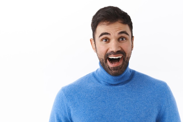 Il ritratto del primo piano dell'uomo caucasico sorridente felice entusiasta con la barba sembra sognante e stupito alla macchina fotografica che contempla qualcosa di bello e di stupefacente fondo bianco in piedi