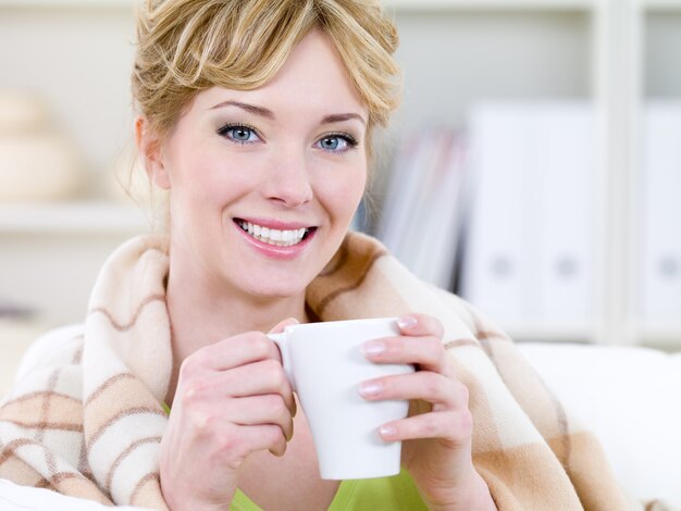 Il ritratto del primo piano di bella giovane donna sorridente felice si riscalda con la tazza di caffè caldo