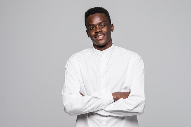 Il ritratto dell'uomo afro sicuro si è vestito in camicia classica bianca con le mani piegate isolate su fondo grigio