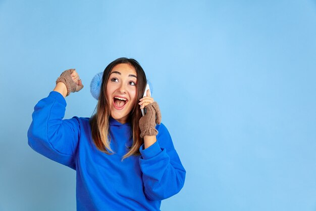 Il ritratto della donna caucasica sullo spazio blu. Bello modello femminile in vestiti caldi