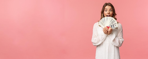 Il ritratto della ragazza fortunata eccitata con il vestito bianco dei capelli biondi vince i soldi riceve il grande lotto del premio in contanti