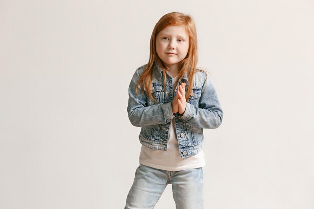 Il ritratto della ragazza sveglia del bambino in jeans alla moda copre l'esame della macchina fotografica e sorridere