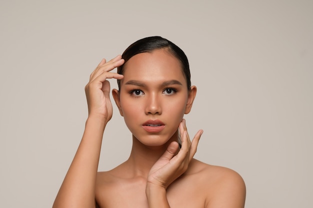 Il ritratto di bella donna asiatica tocca la guancia e la fronte, bella pelle pulita naturale