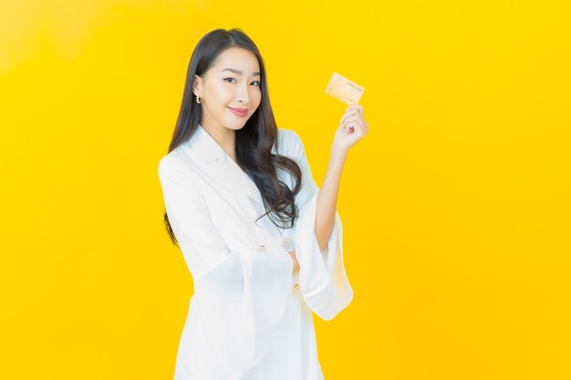 Il ritratto di bella giovane donna asiatica sorride con la carta di credito sulla parete gialla