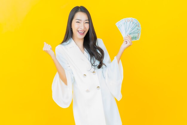 Il ritratto di bella giovane donna asiatica sorride con molti contanti e soldi sulla parete gialla