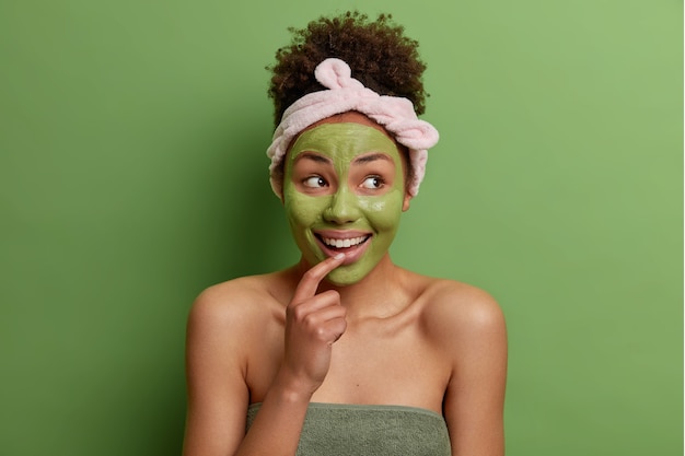 Il ritratto di bellezza del modello femminile felice applica la maschera nutriente verde sul viso