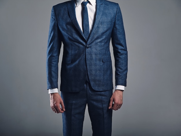 il ritratto di bello modello alla moda dell'uomo d'affari si è vestito in vestito blu elegante che posa sul fondo grigio in studio