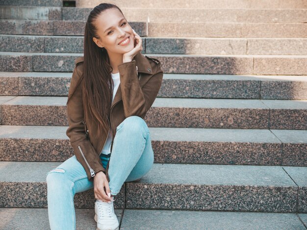 Il ritratto di bello modello castana sorridente si è vestito in vestiti del rivestimento e dei jeans dei pantaloni a vita bassa dell'estate