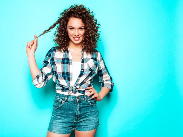 Il ritratto di bello modello sorridente con l'acconciatura dei riccioli di afro si è vestito in vestiti dei pantaloni a vita bassa dell'estate. Donna divertente e positiva alla moda