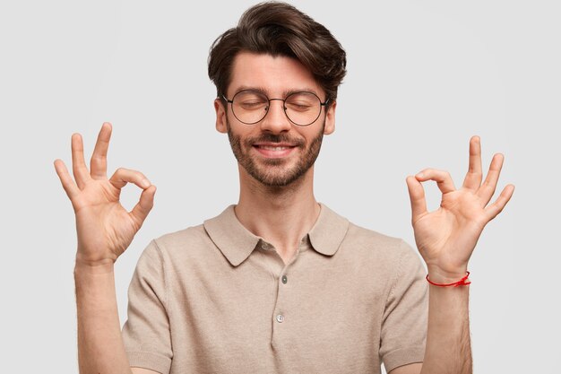 Il ritratto di giovane hipster maschio con la barba lunga felice fa il segno giusto