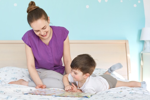 Il ritratto di giovane madre adorabile allegra legge le fiabe per suo figlio