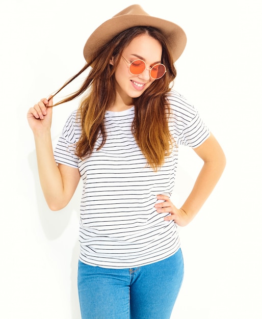 Il ritratto di giovane modello di risata alla moda della donna in estate casuale copre in cappello marrone con trucco naturale isolato sulla parete bianca