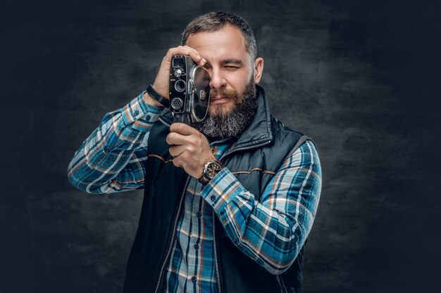 Il ritratto di un maschio barbuto di mezza età tiene una videocamera vintage da 8 mm su sfondo grigio.