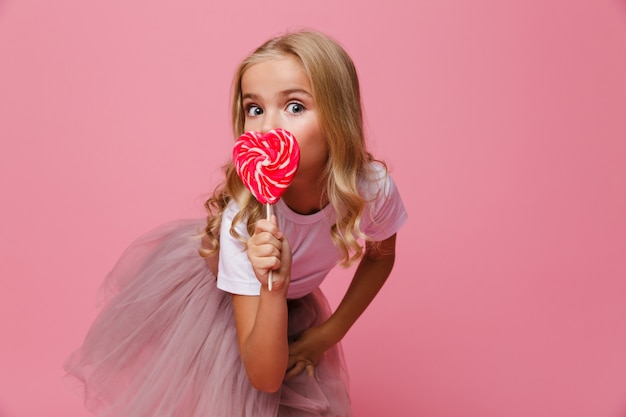 Il ritratto di una bambina graziosa che tiene il cuore ha modellato la lecca-lecca