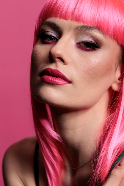 Il ritratto di una donna attraente con l'acconciatura rosa e il trucco alla moda sembra sicuro di posare davanti alla telecamera. Modello sexy spensierato con stile sensuale seduto in studio fotografico.