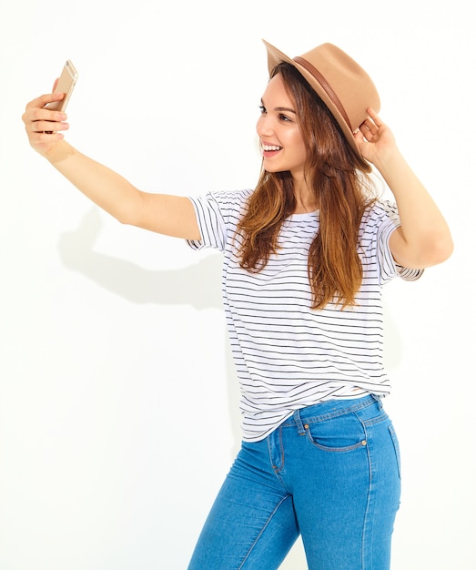 Il ritratto di una donna graziosa in pantaloni a vita bassa dell'estate copre prendere un selfie isolato sulla parete bianca