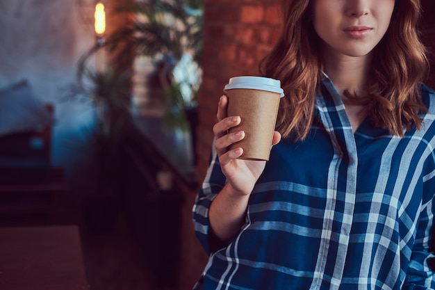 Il ritratto di una ragazza giovane hipster beve il caffè del mattino appoggiandosi a