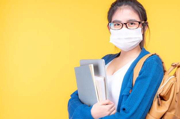 Il ritratto di una studentessa giovane e bella indossa una maschera che tiene un libro di testo - studiando il sistema di e-learning online