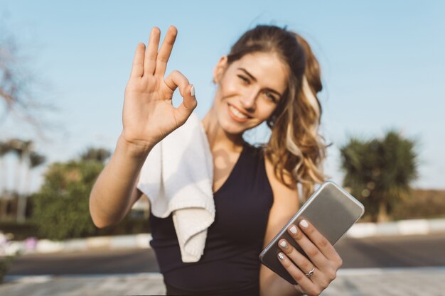 Il ritratto ha motivato la giovane donna felice eccitata in abbigliamento sportivo che sorride, esprimendo positività nella mattina soleggiata all'esterno. Sportiva alla moda, formazione, stile di vita sano