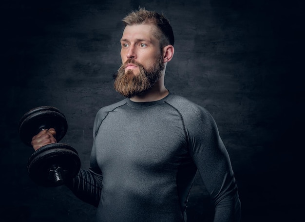 Il ritratto in studio di un maschio barbuto sportivo vestito con un abbigliamento sportivo grigio tiene il manubrio.