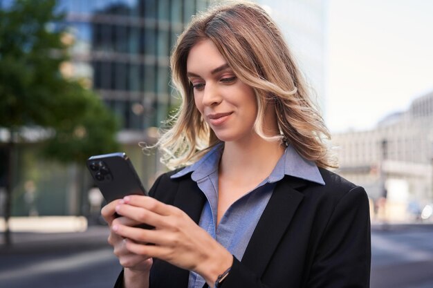 Il ritratto ravvicinato di una giovane donna aziendale in abito nero tiene un messaggio di testo sullo smartphone mentre stan