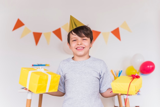 Il ritratto sorridente di un ragazzo che tiene i regali di compleanno in sua mano